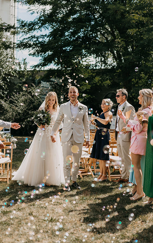 Brautpaar und Gäste während einer freien Trauung hinter Seifenblasen