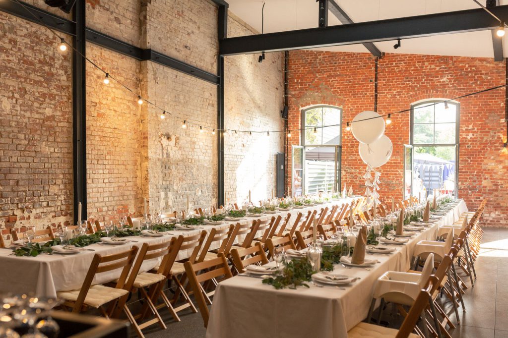 Eine gedeckte Hochzeitstafel mit Klappstühlen ohne Personen in einer Halle