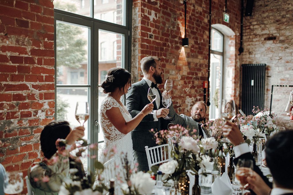 Ein Hochzeitspaar steht an der Tafel und prostet den Gästen zu