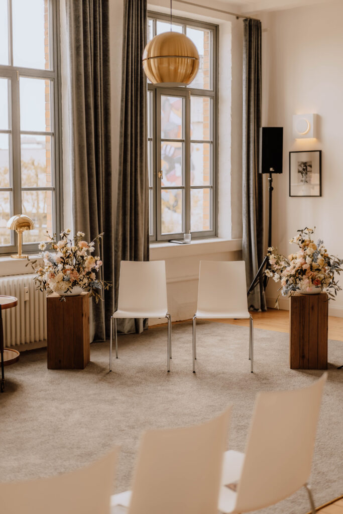 Ein Setting für eine freie Trauung mit weiße Stühlen in einem hellen Loft mit Blumen 